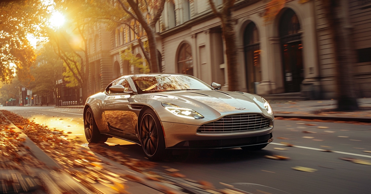 Aston Martin DB11 driving on leaf-covered street in late afternoon sunshine