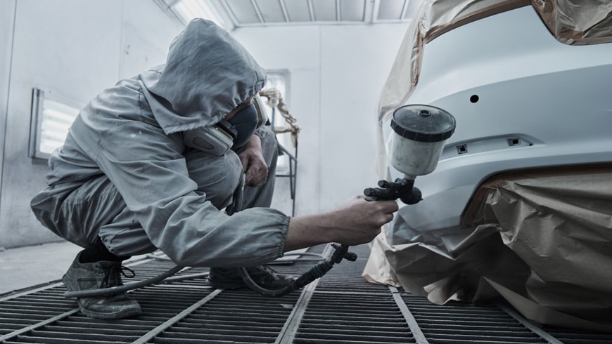 auto body technician spraying primer on car bumper
